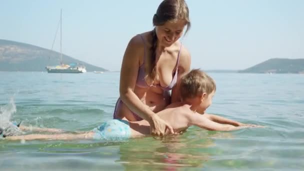 幸せな笑顔の母親は 小さな息子が海で泳ぐことを学んでいます 家族の休日 子供と親の楽しい夏時間 — ストック動画