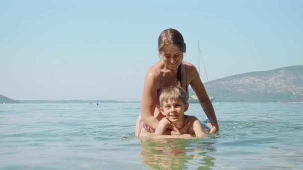 幸せな母親と海で泳ぐことを学ぶ小さな少年 家族の休日 子供と親の楽しい夏時間 — ストック動画