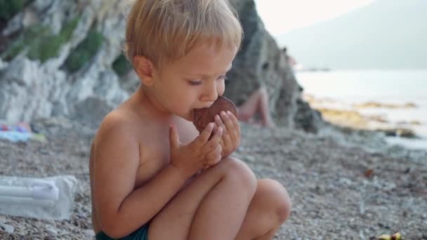 Маленький Хлопчик Сидить Морському Пляжі Їсть Млинці — стокове відео