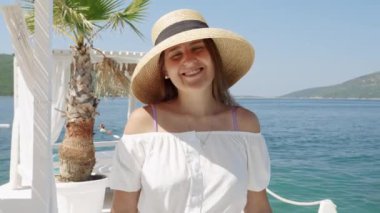 Samandan şapkalı gülümseyen esmer kadının portresi deniz sahilindeki ahşap iskelede yürüyor..