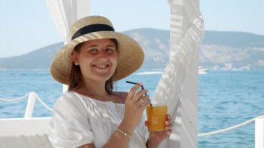 Mutlu, gülümseyen esmer kadının portresi rıhtımdaki plaj kafesinde oturmuş portakal suyu içiyor. Yaz, tatil, dinlenme ve seyahat kavramı