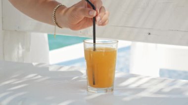 Zarif bir kadının yaz tatilinde deniz kıyısındaki kafe çardakta dinlenirken portakal suyunu samanla karıştırıp içtiği yakın plan..
