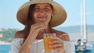 Hasır şapkalı neşeli esmer kadının portresi. Deniz sahilinde portakal suyu ya da kokteyl içiyor..