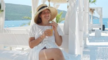 Zarif esmer kadının portresi deniz kıyısındaki restoranda dinleniyor ve yaz tatilinde samanla portakal suyu veya kokteyl içiyor..