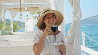 Deniz kenarındaki bir kafede genç esmer kadın kahvesini içip deniz dalgalarını seyrediyor. Yaz tatillerinin, tatillerin, seyahatlerin, seyahatlerin ve deniz seyahatlerinin keyfi.