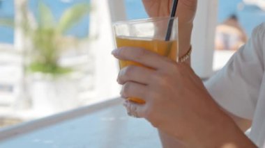 Sahildeki bir kafede, bir kadın portakal suyu içer, yaz tatillerini ve kıyı rahatlığını simgeler..