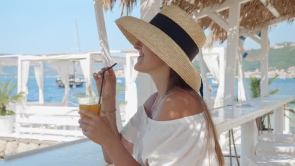 海によって 女性はオレンジジュースを飲み および沿岸の楽しみをカプセル化します — ストック動画