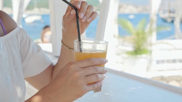 Ένα Παραθαλάσσιο Καφέ Μελαχρινή Γυναίκα Ανακατεύοντας Και Πίνοντας Χυμό Πορτοκάλι — Αρχείο Βίντεο