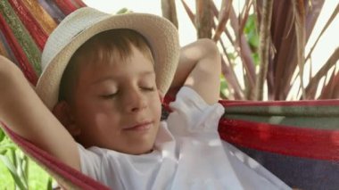 Şapkalı neşeli bir çocuk bahçe hamağında dinlenir, yazın özünü yakalar, mutlu bir çocukluk ve mutlu bir tatil geçirir..