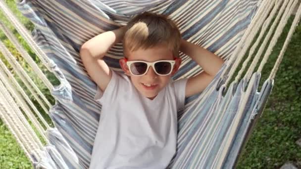 Spokoju Ogrodzie Chłopiec Okularach Przeciwsłonecznych Huśta Się Wypoczywa Hamaku Wyrażając — Wideo stockowe
