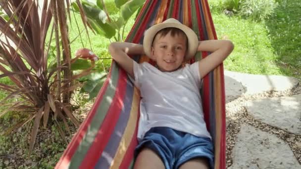 男の子は庭で笑顔でハンモックで泳ぎ 夏の気持ち 幸せな子供時代 リラクゼーション 休暇の魅力をキャプチャします — ストック動画