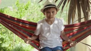 Tatil titreşimleri: Şapkalı çocuk bahçe hamağında dinleniyor, kaygısız anıların tadını çıkarıyor..