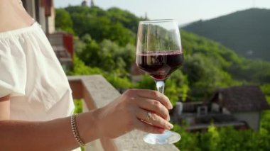 Dağlardaki villanın balkonunda dikilirken kırmızı şarap kadehini tutan kadının yakın çekimi..