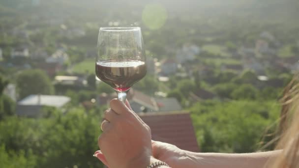 年轻女子 她优雅地捧着那杯红酒 面对着从别墅阳台或阳台上落山的背景 — 图库视频影像