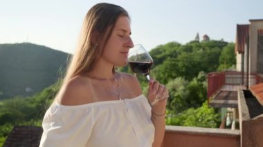 Dağlardaki balkonda ya da villa terasında dikilirken camdan kırmızı şarap içen zarif esmer kadının yakın çekimi. Şarap, bayram kutlaması, yaz tatili.