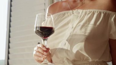 Esmer bir kadının, büyüleyici bir günbatımında, villa terasında ya da balkonda beklerken bir bardak kırmızı şarabın tadını çıkarırken yakın çekimi.