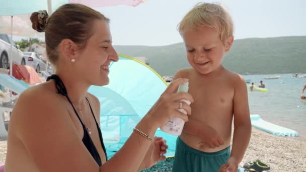 Jovem Mãe Aplicando Spray Protetor Solar Seu Filho Bebê Enquanto — Vídeo de Stock