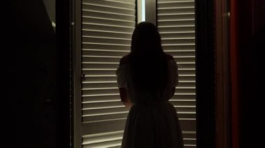 Uzun elbiseli genç esmer kadın balkon kapılarını açar, terasta yürür ve dağların üzerinden güneşin doğuşunu veya batışını seyreder. Yaz tatili, tatil, doğa ve seyahat kavramı