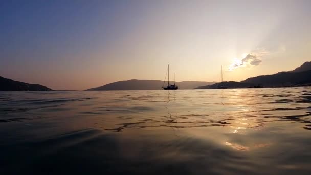 穏やかな海面から眺める夕日空と山の背景を持つヨットのシルエットのゆっくりとした動き — ストック動画