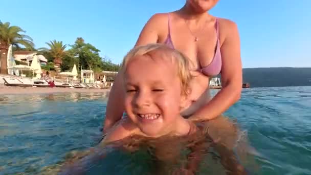 夏休み中に母親と一緒に泳ぐことを学ぶ 笑顔と喜びで満たされた子供としてビーチで楽しい家族の休日をお楽しみください — ストック動画