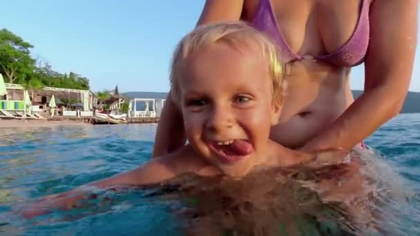 夏の間に母親から水泳のレッスンを受けながら笑いを止めることができない楽しい幼児と家族のビーチ休暇の最後の思い出 — ストック動画