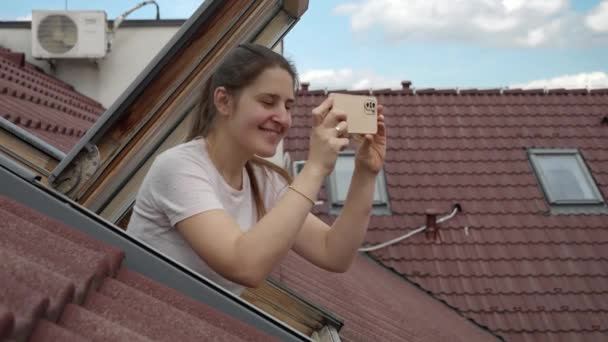 オープンな窓から外を見つめ スマートフォンで写真を撮る若い笑顔の女性 観光のコンセプト ヨーロッパでの休日 旅行や旅 — ストック動画