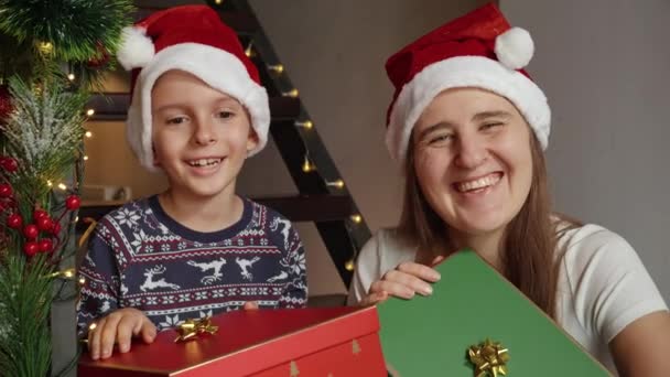 Szczęśliwy Wesoły Uśmiechnięty Chłopiec Matką Gospodarstwa Prezenty Świąteczne Mikołaja Siedząc — Wideo stockowe