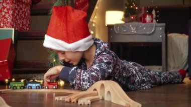Noel Baba 'dan hediye olarak alınan tahta demiryolu ve trenle oynayan pijamalı küçük çocuk. Kış tatili, kutlamalar ve parti.