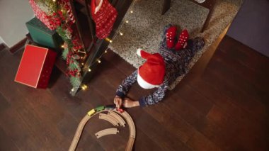 Pijamalı, yerde uzanmış oyuncak ahşap tren ve demiryollarıyla oynayan tatlı çocuk Noel 'i ya da yeni yılı kutluyor. Kış tatili, kutlamalar ve parti.