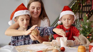 Gülümseyen genç anne, oğullarına mutfakta Noel kurabiyesi yapmayı öğretiyor..