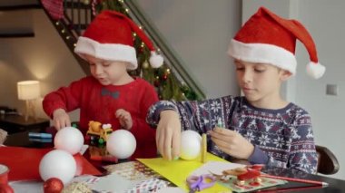 Noel Baba şapkalı iki çocuk kış tatili için geleneksel el yapımı Noel süsleri ve takılar yapıyorlar..