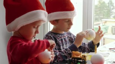Noel Baba şapkalı iki neşeli çocuğun portresi geleneksel Noel süsleri, çelenkler ve takılar yaparken yaratıcı oluyor. Kış tatili, aile zamanı, aileleri kutlama yapan çocuklar.