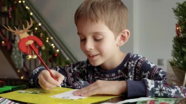 Pijamalı küçük bir çocuğun Noel Baba 'ya dilekleriyle bir mektup yazması.