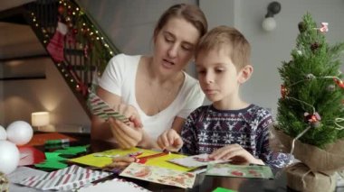 Annesiyle mutlu çocuk kış tatiline hazırlanırken el yapımı Noel kartpostalları ve tebrik kartları hazırlıyor. Kış tatili, aile zamanı, aileleri kutlama yapan çocuklar.