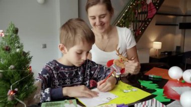 Mutlu gülümseyen anne oğluna bakıp Noel Baba 'ya mektup yazıyor. Kış tatili, aile zamanı, aileleri kutlama yapan çocuklar.