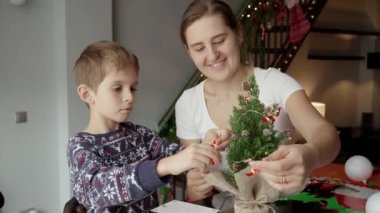 Annesi küçük Noel ağacını çelenk ve ışıklarla süsleyen mutlu küçük bir çocuk. Kış tatili, aile zamanı, aileleri kutlama yapan çocuklar.