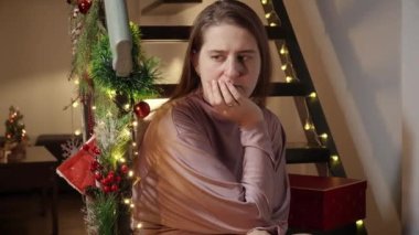 Düşünceli, üzgün ve üzgün bir kadının portresi Noel için süslenmiş ahşap merdivenlerde oturup misafirleri bekliyor. Kutlamalarda olumsuz duygular, depresyon ve yalnızlık