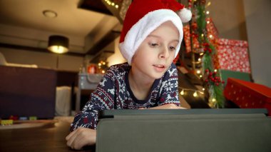 Noel Baba şapkalı küçük çocuk yerde yatıyor ve Noel 'de tablet bilgisayar kullanıyor..