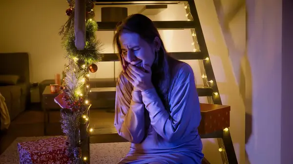 Police or ambulance car lights illuminating face of crying young woman sitting on wooden stairs decorated for Christmas or New Year. Crime, ambulance, injury, problems with law and theft on winter holidays and celebrations