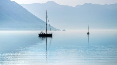Sabah sisi ve sisle dolu sakin deniz limanına demirlemiş iki yatın silueti..