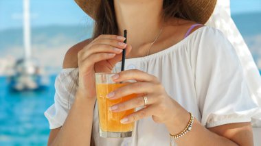 İskeledeki bir plaj kafe çardağında esmer bir kadın saf zevkle portakal suyunun tadını çıkarıyor. Yazın özü, tatil sükuneti, rahatlama ve seyahat çağrısı..