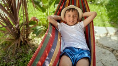 Bir çocuk sallanır ve bahçede gülümseyerek bir hamakta dinlenir, yaz mevsiminin hislerini yakalar, mutlu bir çocukluk, rahatlama, ve bir tatilin cazibesi.