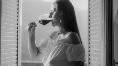 Zarif bir kadının siyah beyaz portresi Dağ köşkünün kapısında kırmızı şarap içiyor.