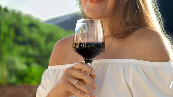 Closeup video clip, showcasing an elegant lady sipping red wine from a glass on a charming villa terrace, set against the stunning backdrop of mountainous landscapes.