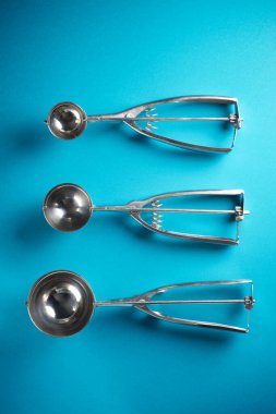 Mavimsi yeşil bir masada üç farklı boyutta dondurma kepçesi.