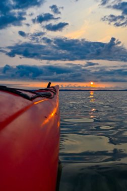 29 Haziran 2023 'te Vattern Motala Gölü üzerinde turuncu gün batımında kırmızı bir kano.