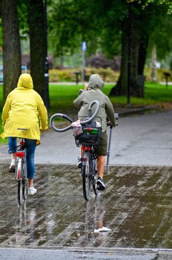 Bisikletiyle yağmurda sepette elektrikli süpürgeyle gezer. İsveç 'te yağmurlu bir günde. 9 Ağustos 2023.