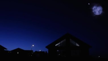 Günbatımında Ay 'la birlikte bir evin silueti ve arka planda düşen bir meteor..  