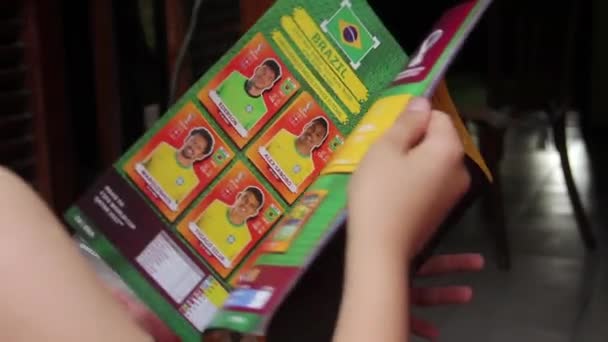 2022 Fifaワールドカップカタールオフィシャルステッカーアルバムを見る少年 クローズアップ ソリューション — ストック動画