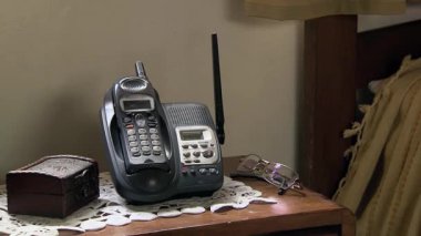 Yatağın kenarındaki masadaki kablosuz telefon Yaşlılar Odasında Kişisel Ögelerle çevrili - Kapat - 4K Çözünürlük